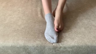 The girl caresses her legs and takes off her socks with her feet